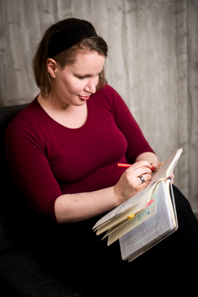 Eine Frau sitzend mit einem Notizbuch in der Hand und einem Füller in der rechten.